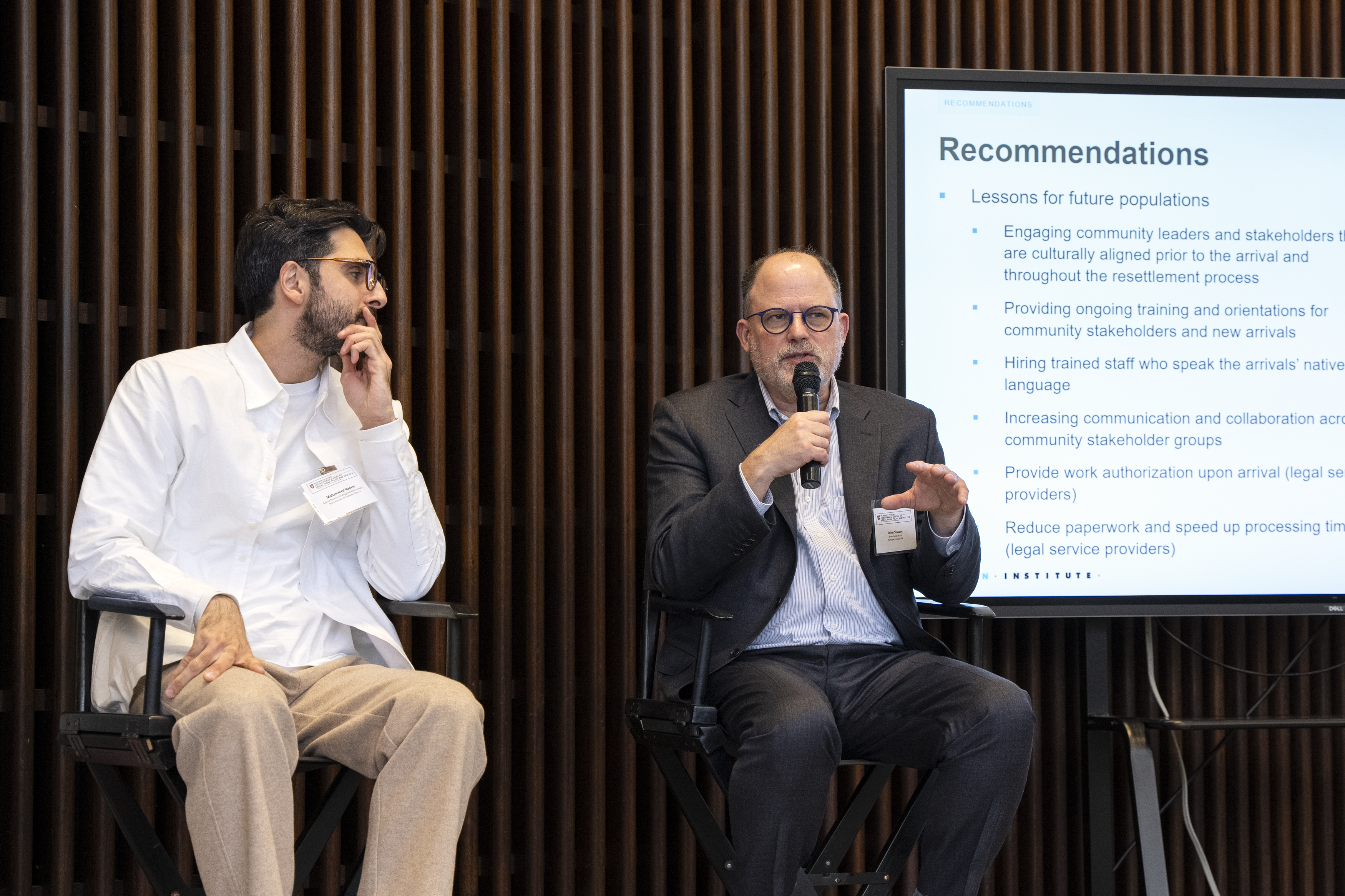 image of man in white shirt sitting in a director chair listening to another man in a blue suit talking on a microphone