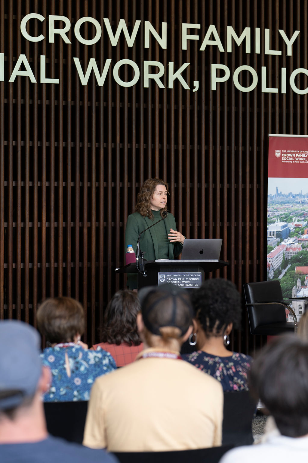 Woman in dark green blazer stands at podium talking