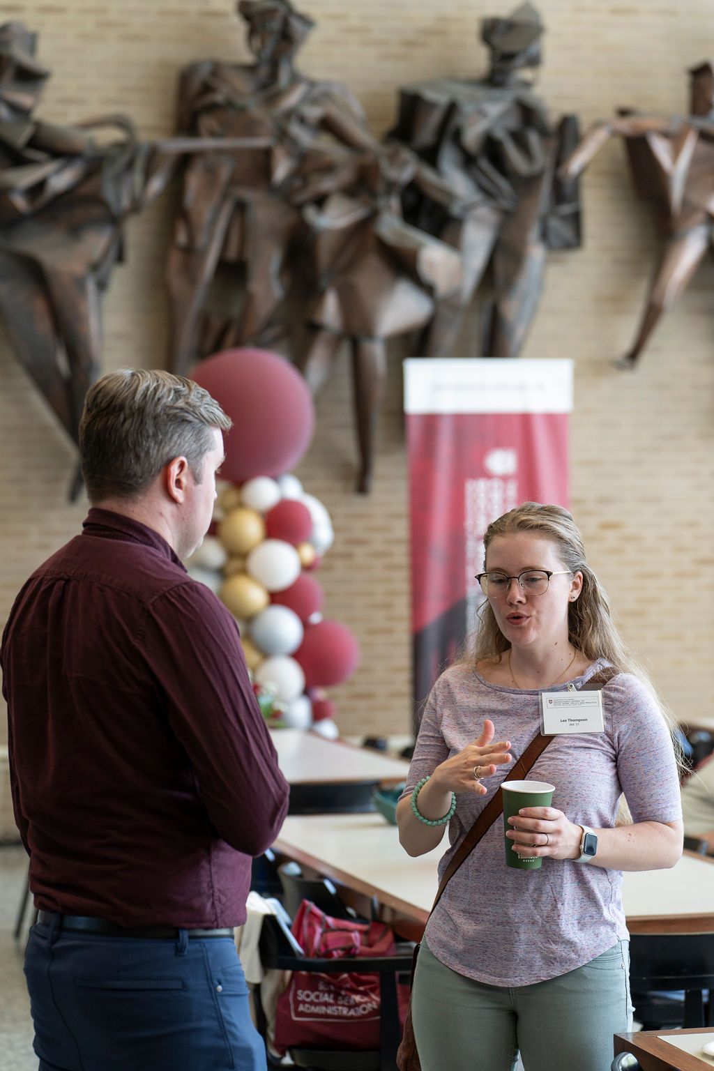 A man in a maroon shirt talks with a woman in a lavender shirt standing