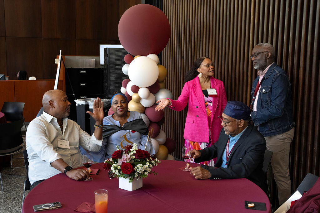 Five people gathered around a table with balloons talking