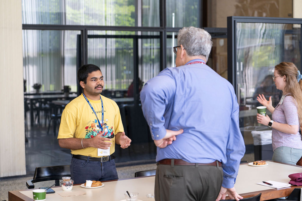 Two men standing talking one in yellow shirt the other in blue shirt 