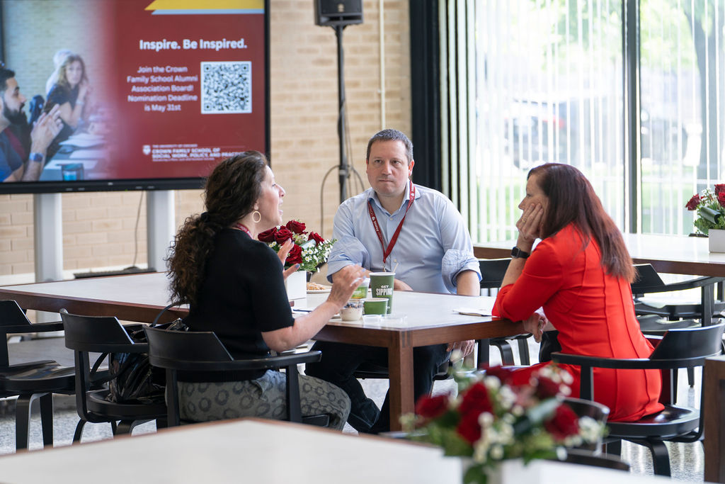 Three people sit at a table talking 