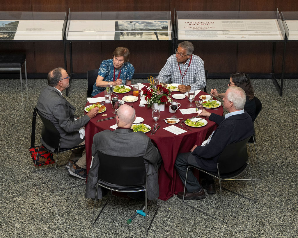 Six people seated at a round table eating dinner during a party