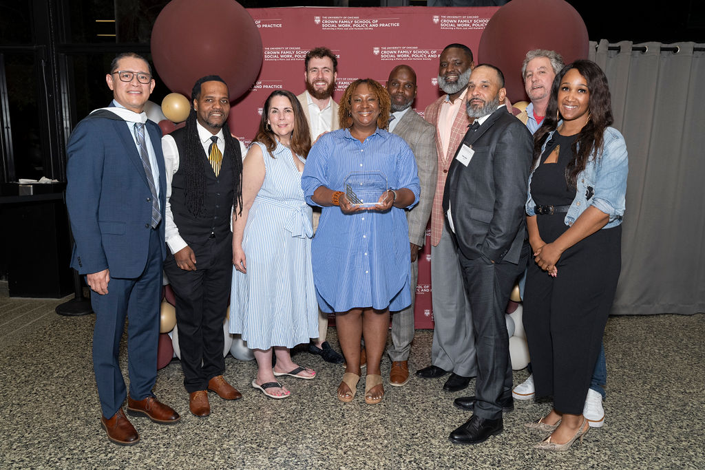 group of people all smiling in front of a step and repeat with balloons holding an award