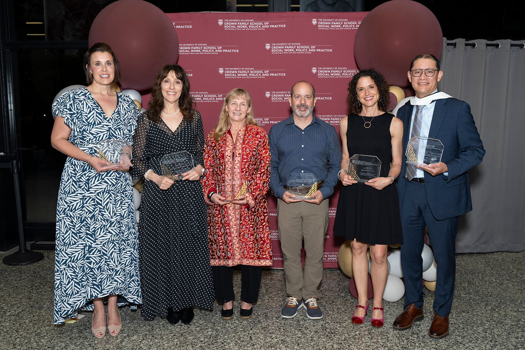 group of people stand smiling holding awards in front of a step and repeat