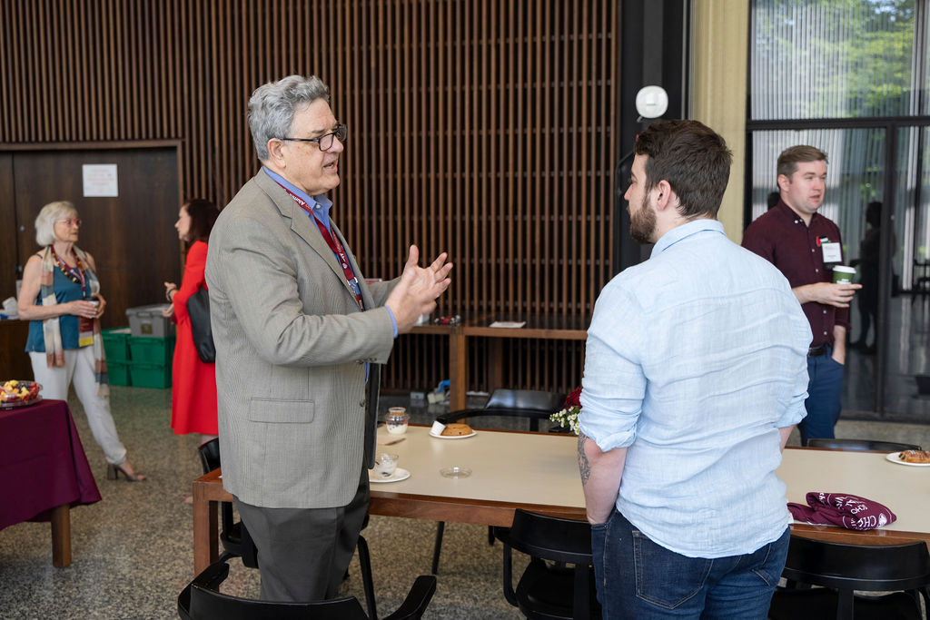 Two male presenting people talk near tables