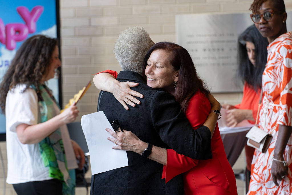 Two women embrace while women stand in the background looking on