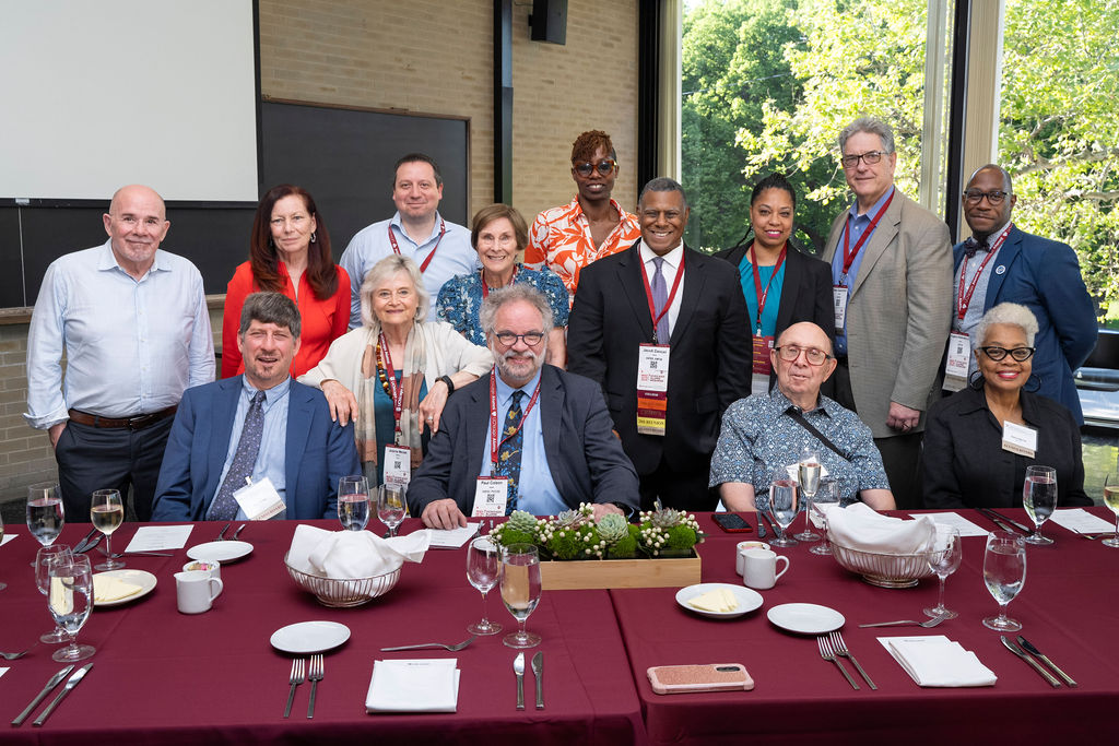 A group of people sitting and standing at dinner table smile towards the camera