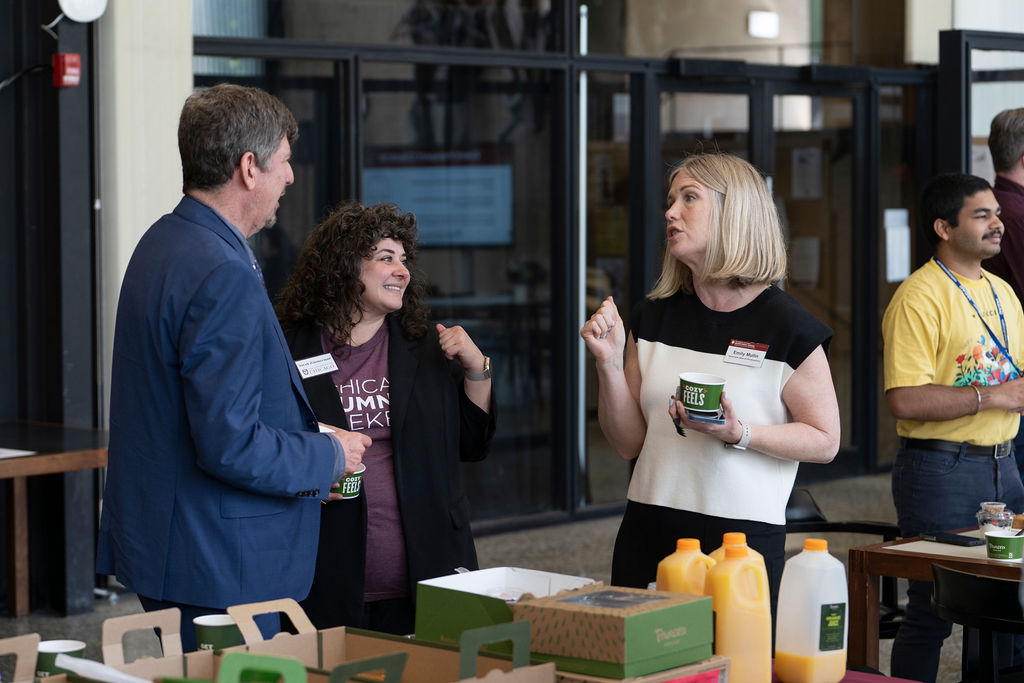 Three people stand near table with snacks talking