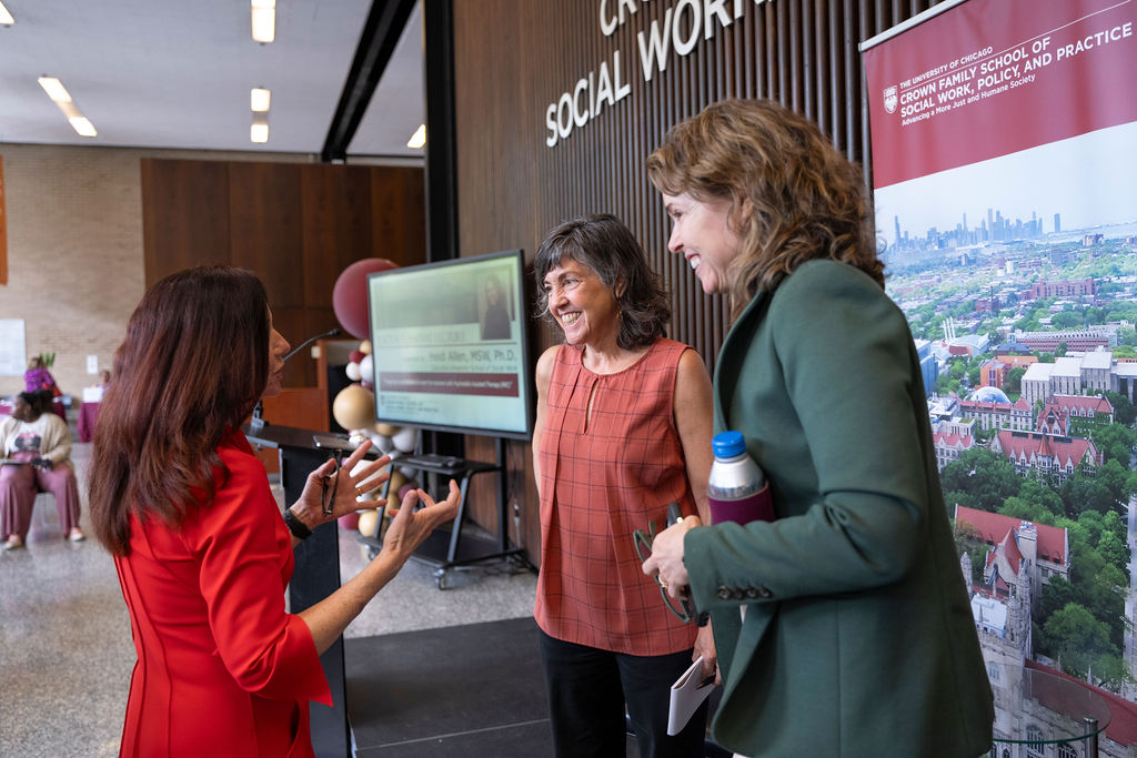 Two women stand smiling and listening to a third talking