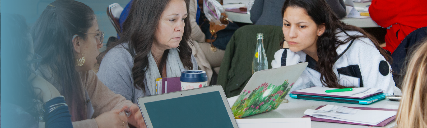 Image of a woman on a laptop sitting at a table working collaboratively with two others 