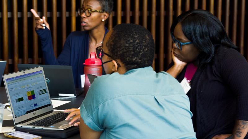 Image of a woman in a blue sweater sitting a table working collaboratively with two others