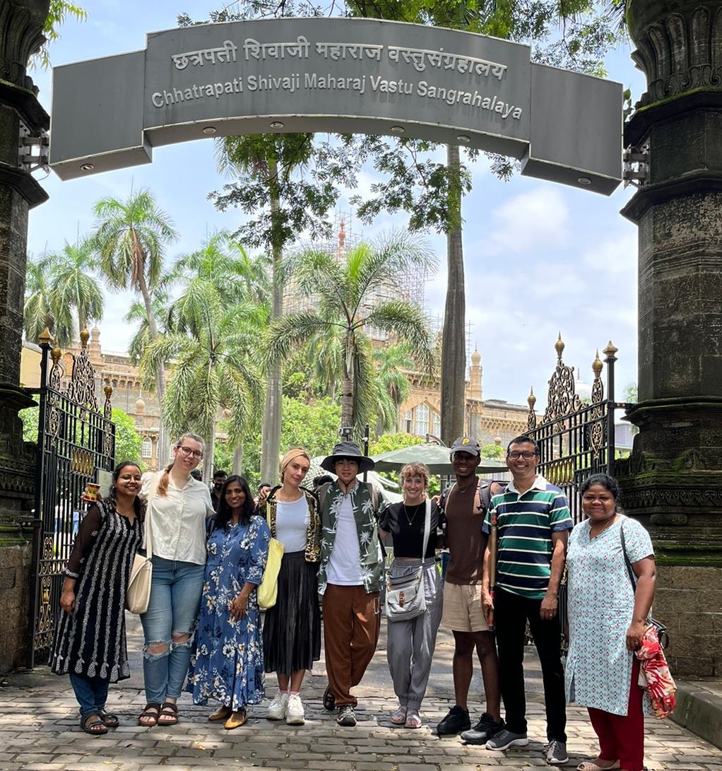 group of nine people standing together smiling in front of a sign 