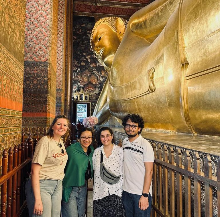 a group of 4 people standing smiling in front of a golden sculpture