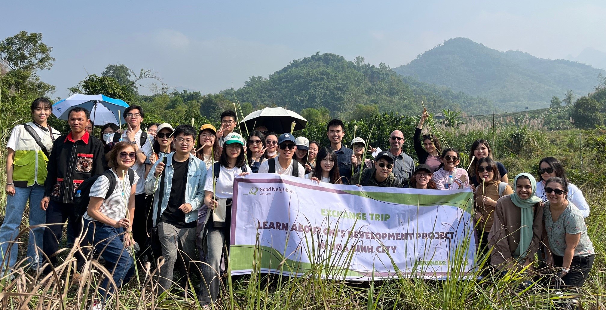 a large group of students in a grassy area holding a banner for an exchange trip