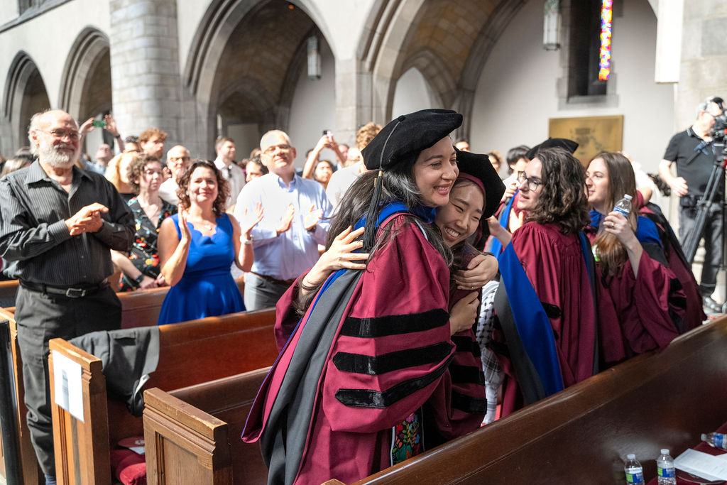 Two PhD candidates hug during their graduation hooding ceremony.