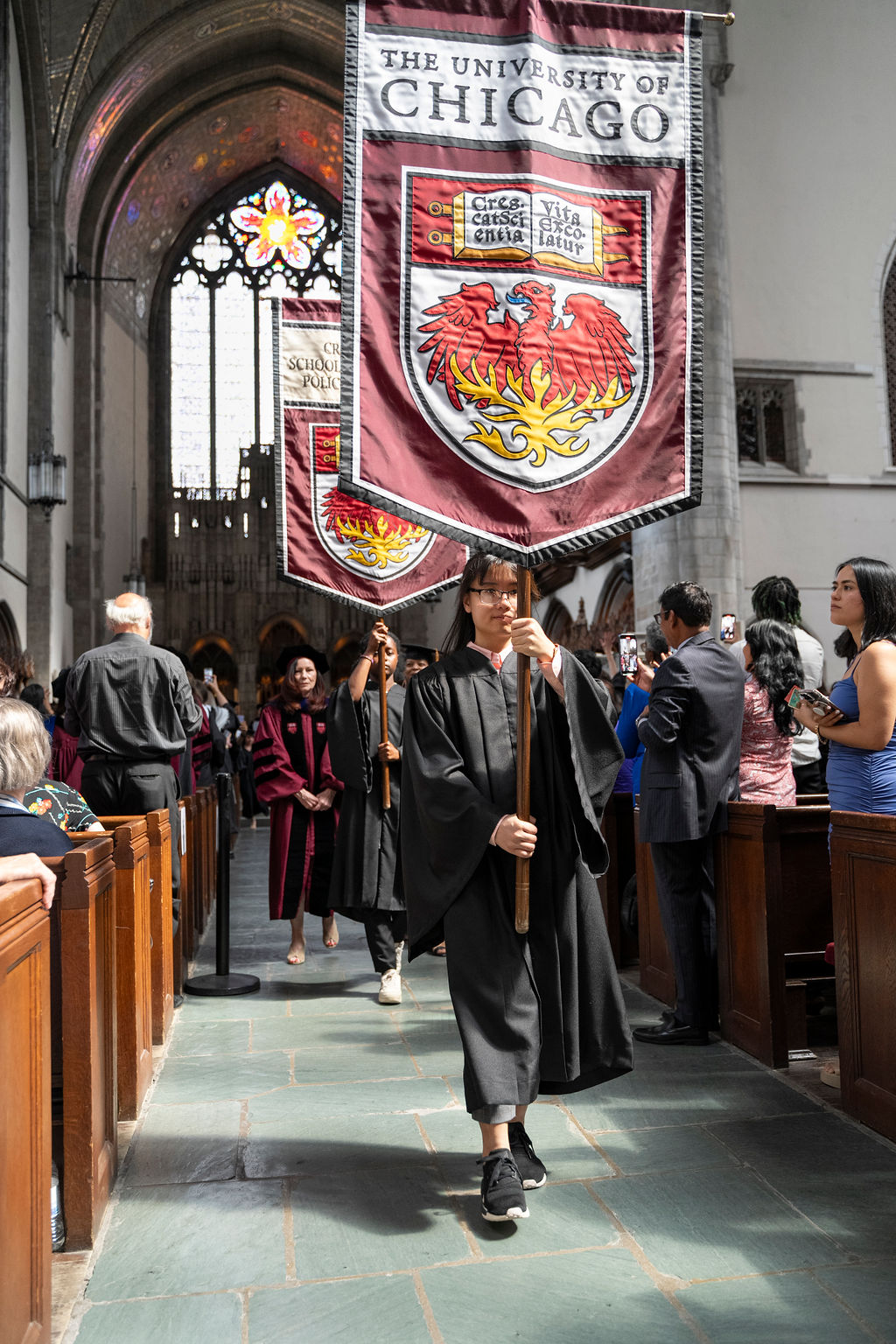 Flag bearers walk down the aisle carrying the University of Chicago banner during a hooding ceremony