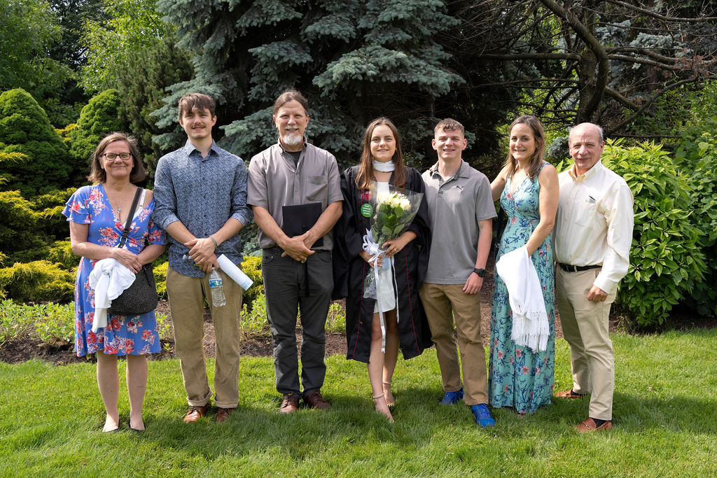 A family takes a group photo with the graduate in the middle holding flowers 