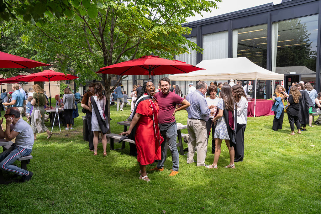 Reception following hooding ceremony gets underway as attendees enjoy nice weather on the lawn under yard umbrellas 