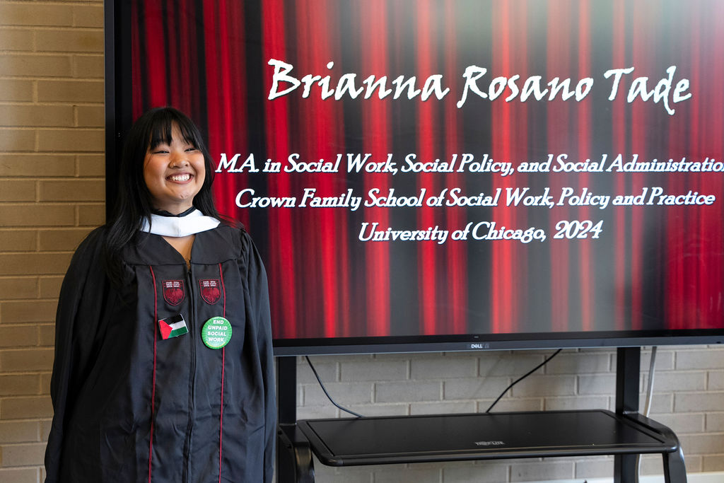 Graduate stands next to monitor displaying her name during a reception following the hooding ceremony