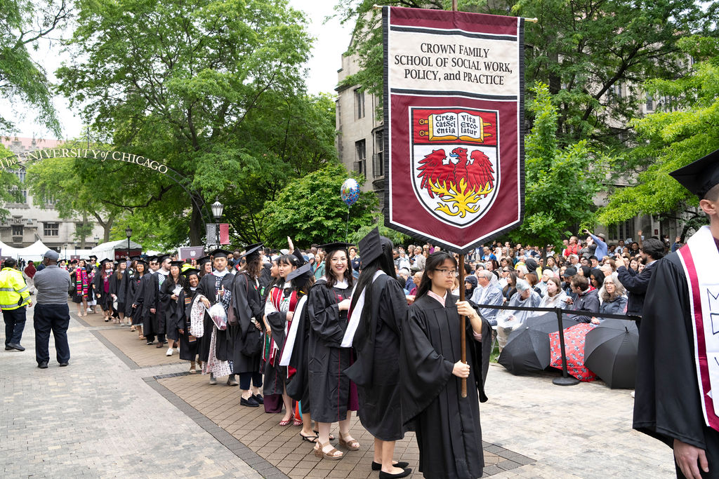 Graduates line up for Convocation processional front person carrying Crown Family School banner