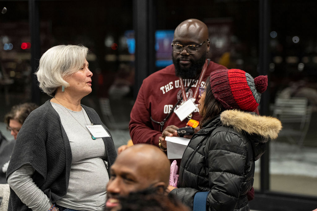 man in a maroon sweatshirt talking with a woman in a grey sweater with a namebadge