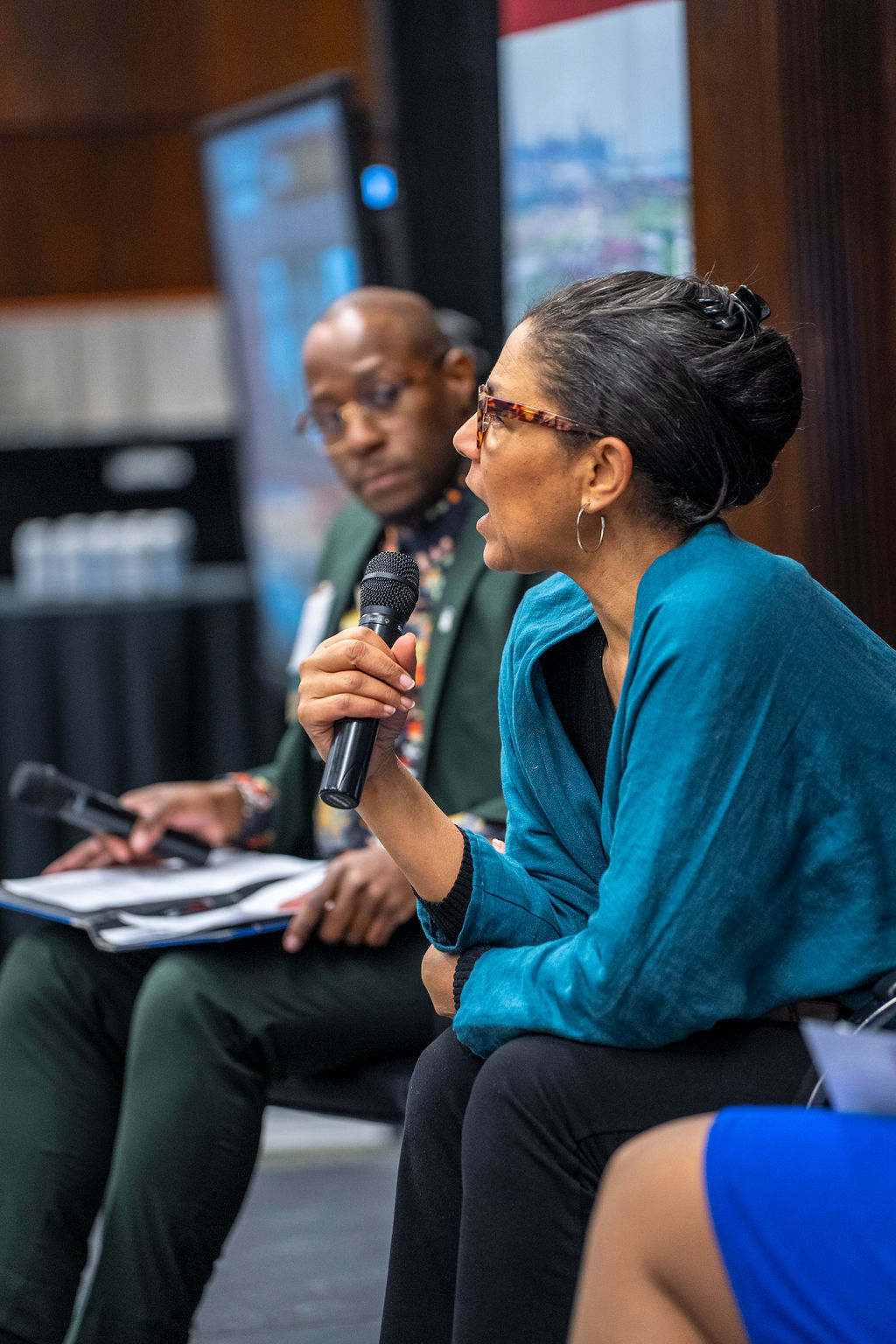 Close shot of woman in blue and black with glasses speaking with microphone.