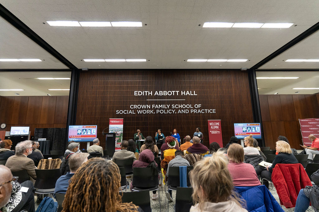 Far shot of the crowd and panelists on stage with Edith Abbott Hall wall in the background.