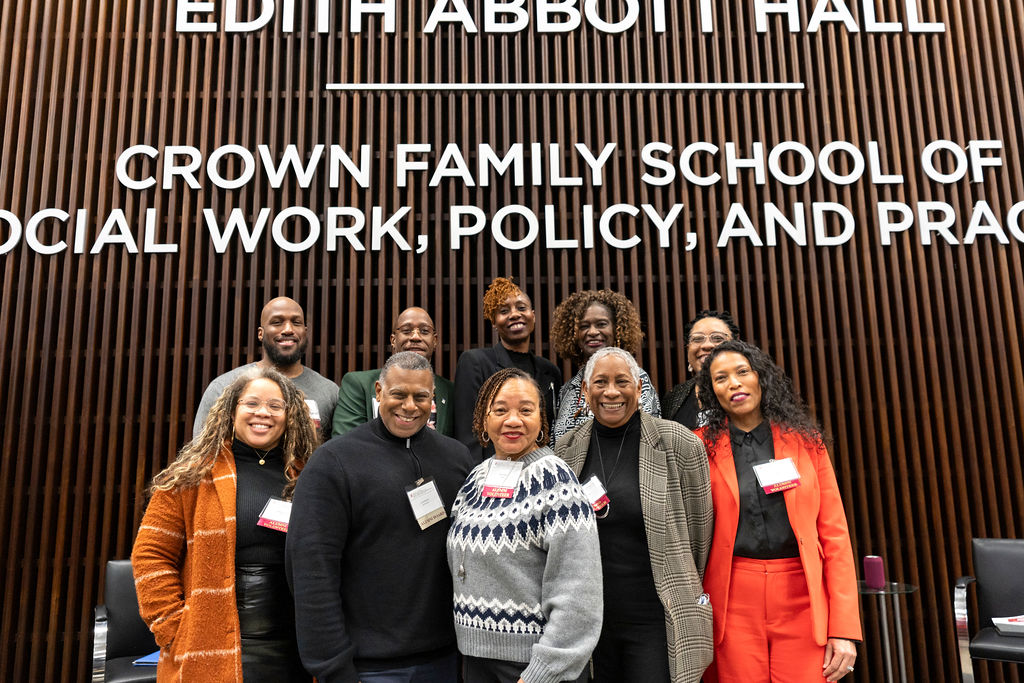 A group of people standing in front of a Social Work School sign with badges smiling