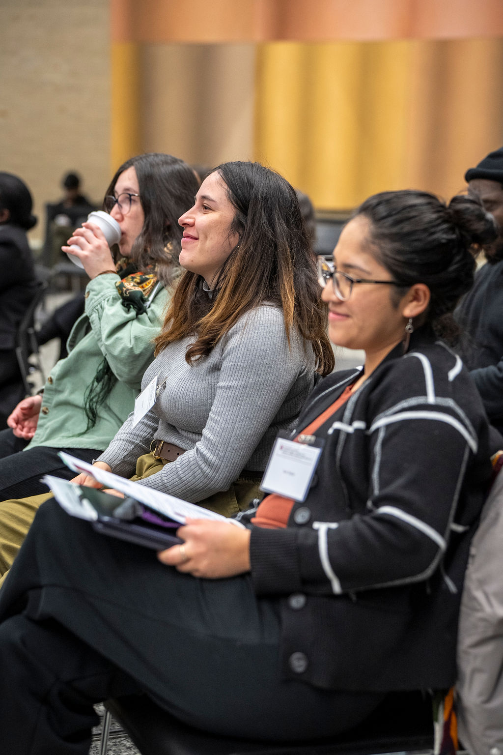 3 women crowd members. One drinking and the others smiling.