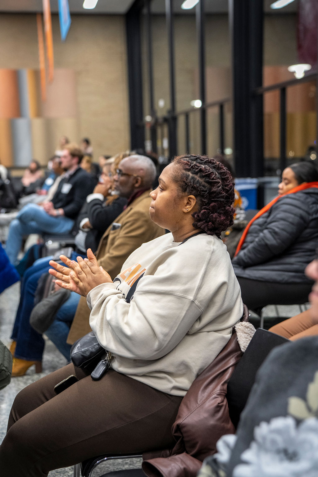Shot of black woman in crowd in grey sweater clapping her hands. 
