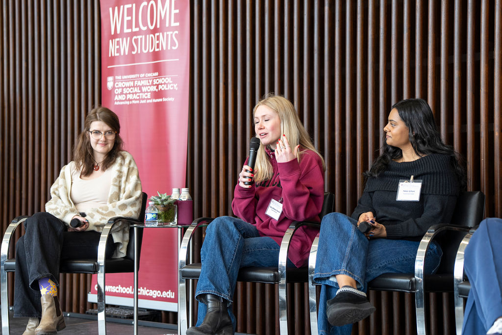 Woman in light colored cardigan looking over with woman in black sweater towards woman in red sipper jacket.