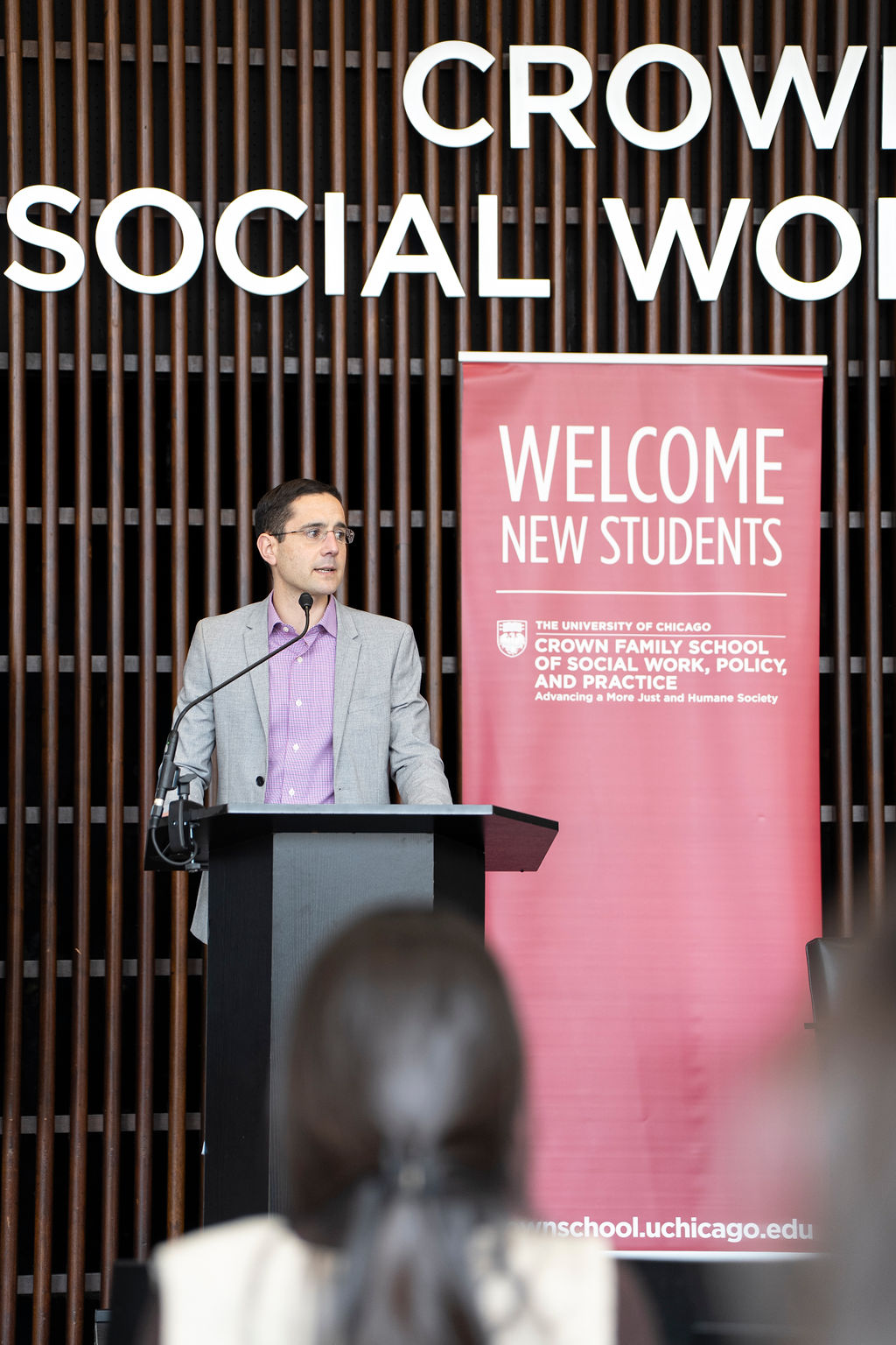 Man in grey suit jacket looking off to the side as they stand behind a podium.