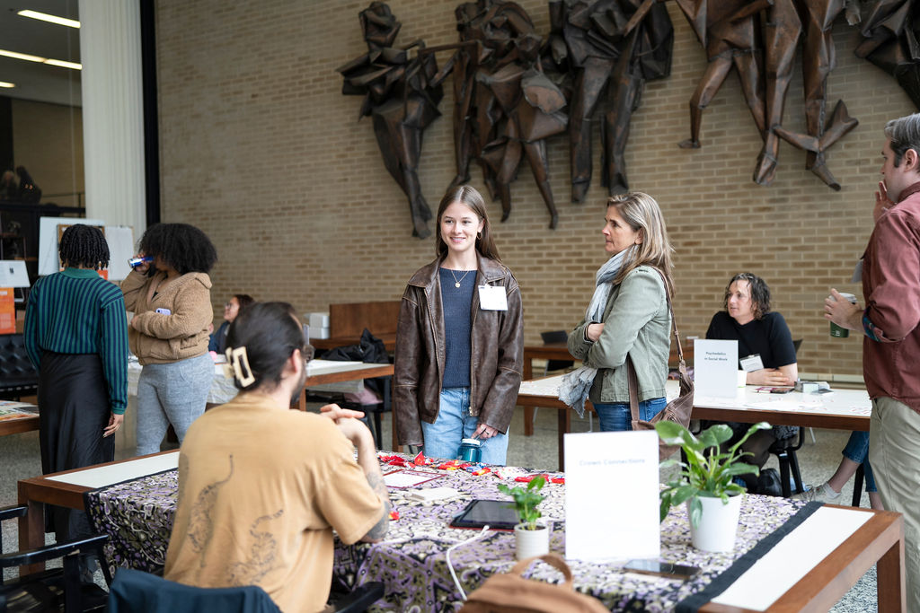 Woman in brown jacket smiling and woman in green jacket standing in front of table 