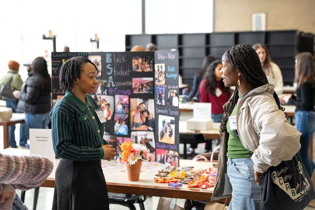 Black woman in green striped shirt talking to black woman with twists in font of black student association table
