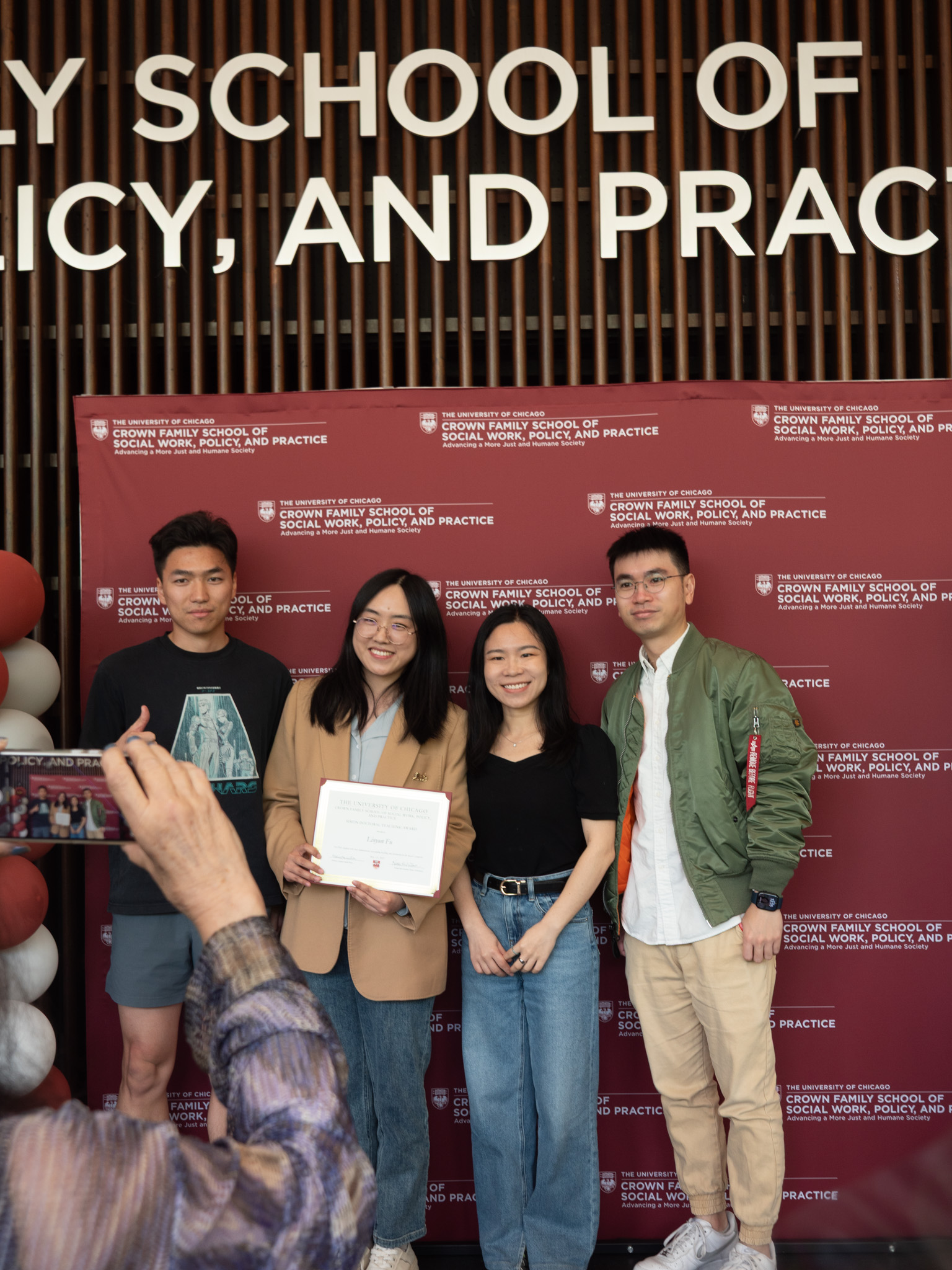 Student awardee wearing brown blazer taking a picture with three others in front og backdrop