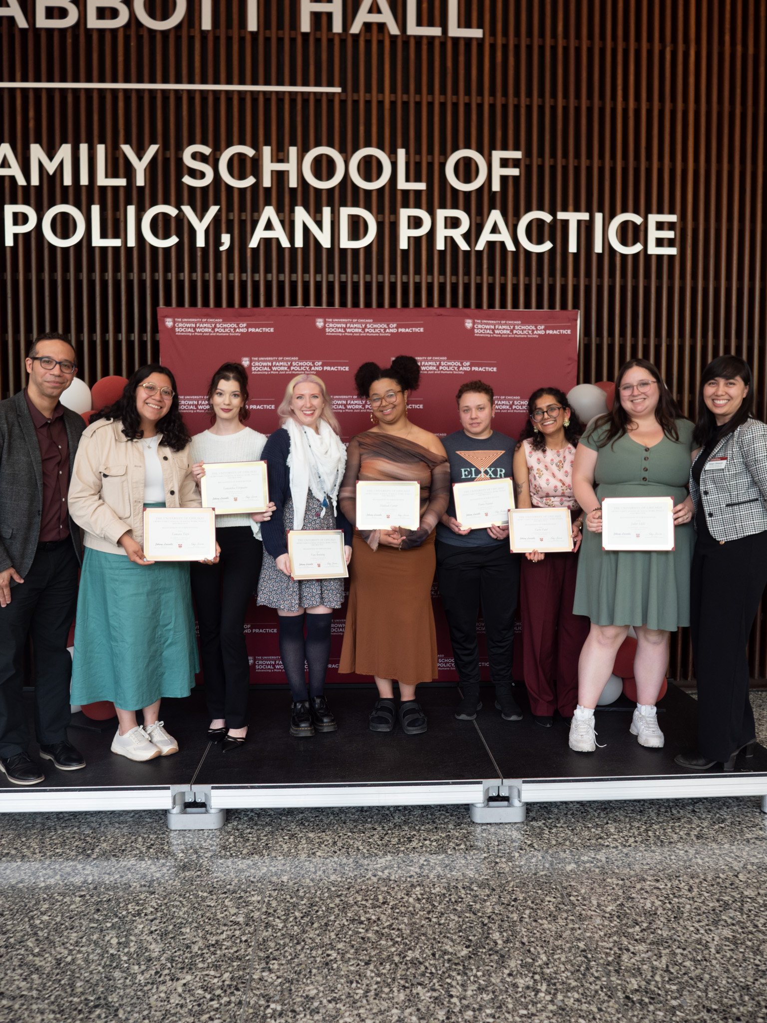 Students holding awards taking a picture in front of backdrop and balloons