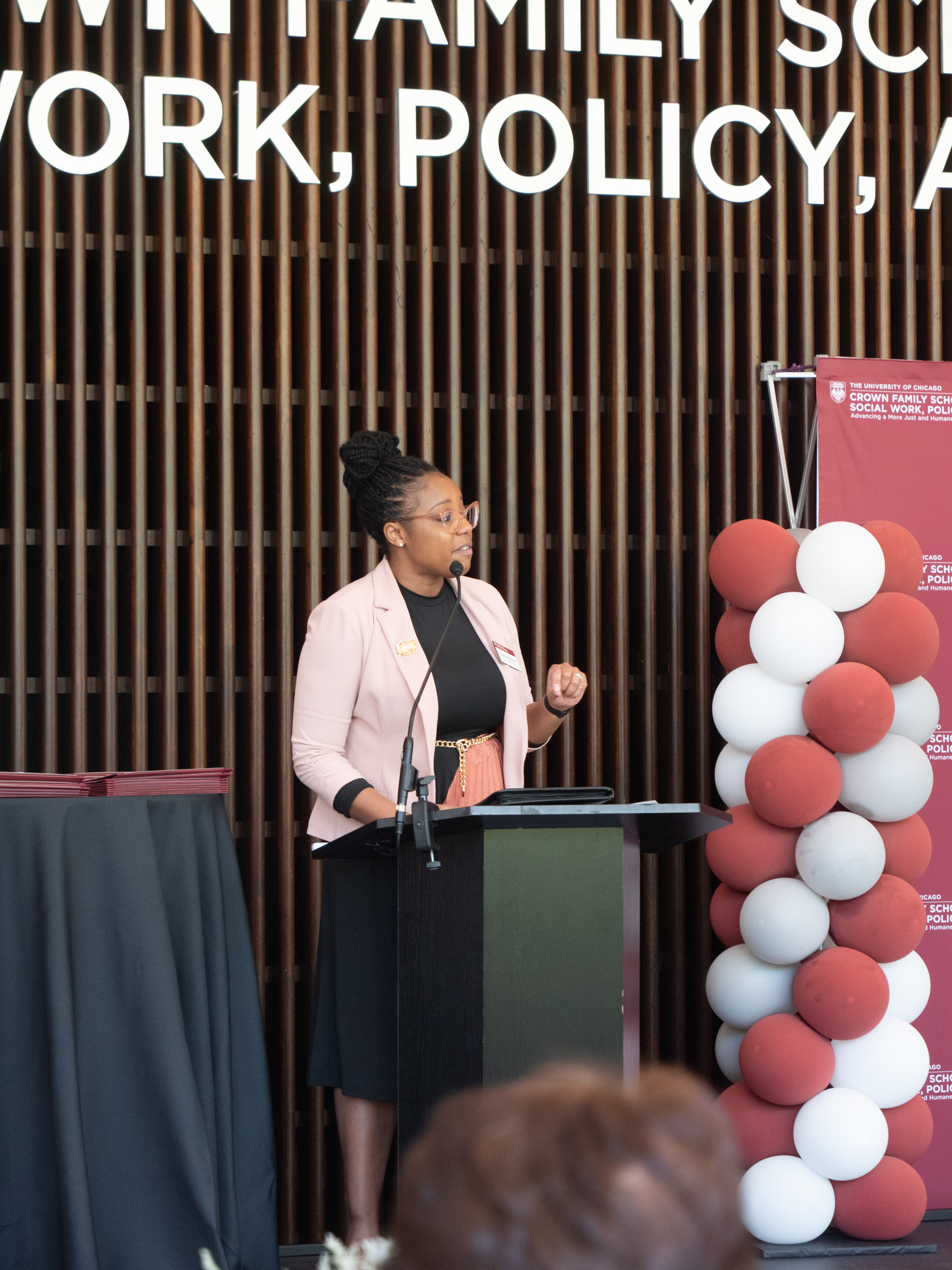 Black woman wearing pink blazer speaking behind the podium