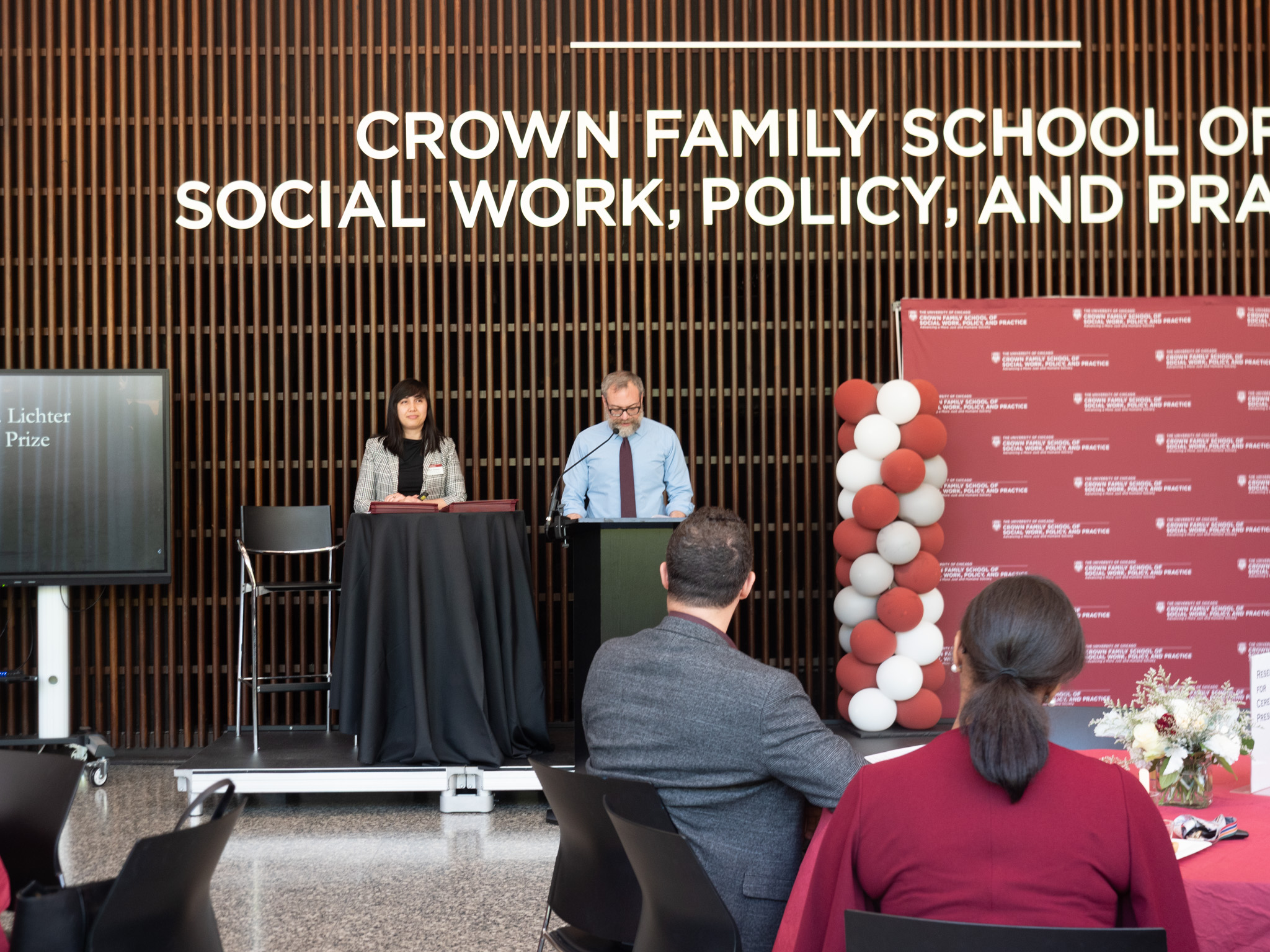 Man in blue shirt and maroon tie speaking behind podium