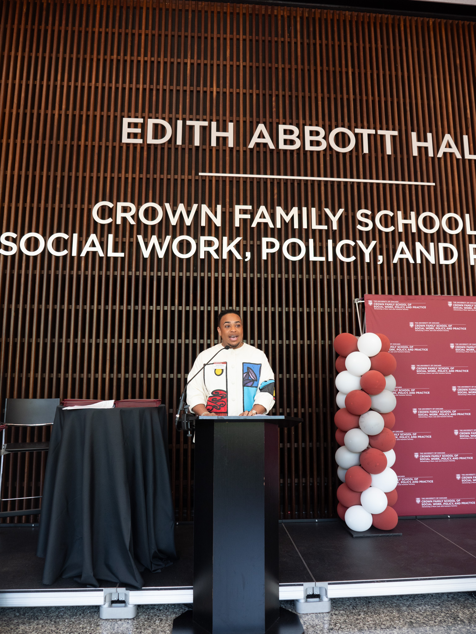 Black man wearing white with colorful patterns speaking behind podium
