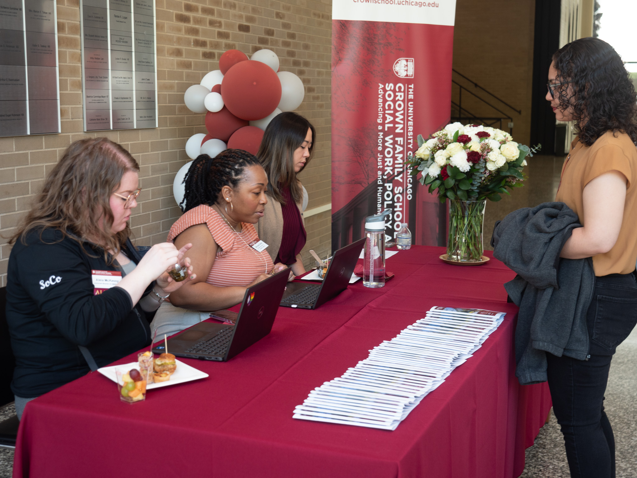 Woman standing in front of table with pamphlets on it and three women with laptops behind it 