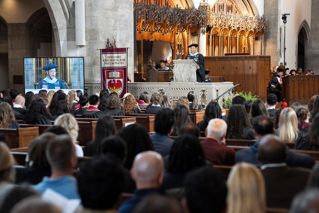Image of a female in black regalia speaking at a podium with image also on the monitor