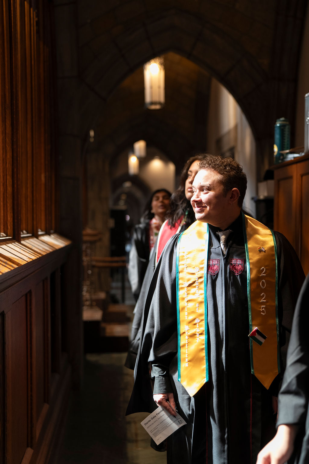 graduate in black robe with gold and green stole looking out smiling 