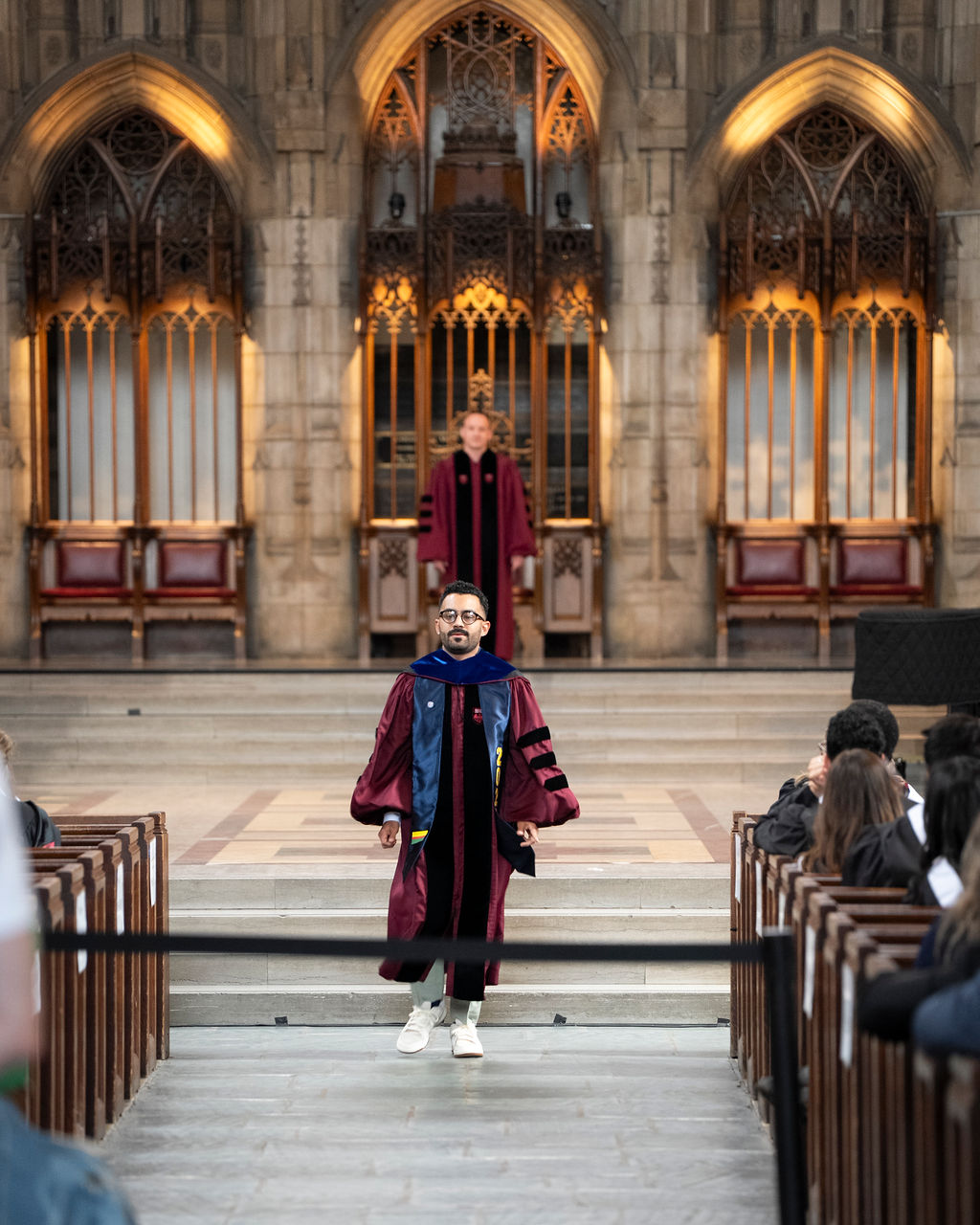 two graduates in maroon robes walk in a chapel 