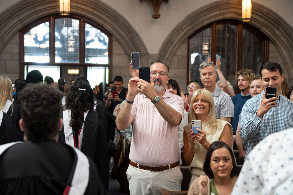 image of a group of people holding phones to capture images of graduates processing out