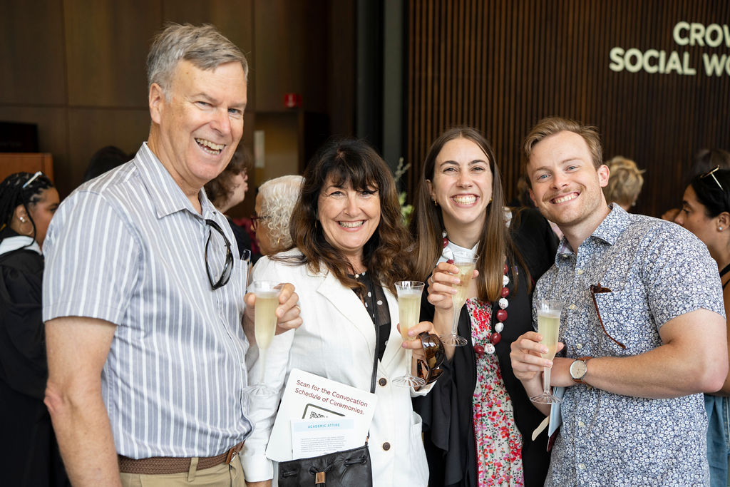 four people standing with champagne with a graduate in a black robe all smiling