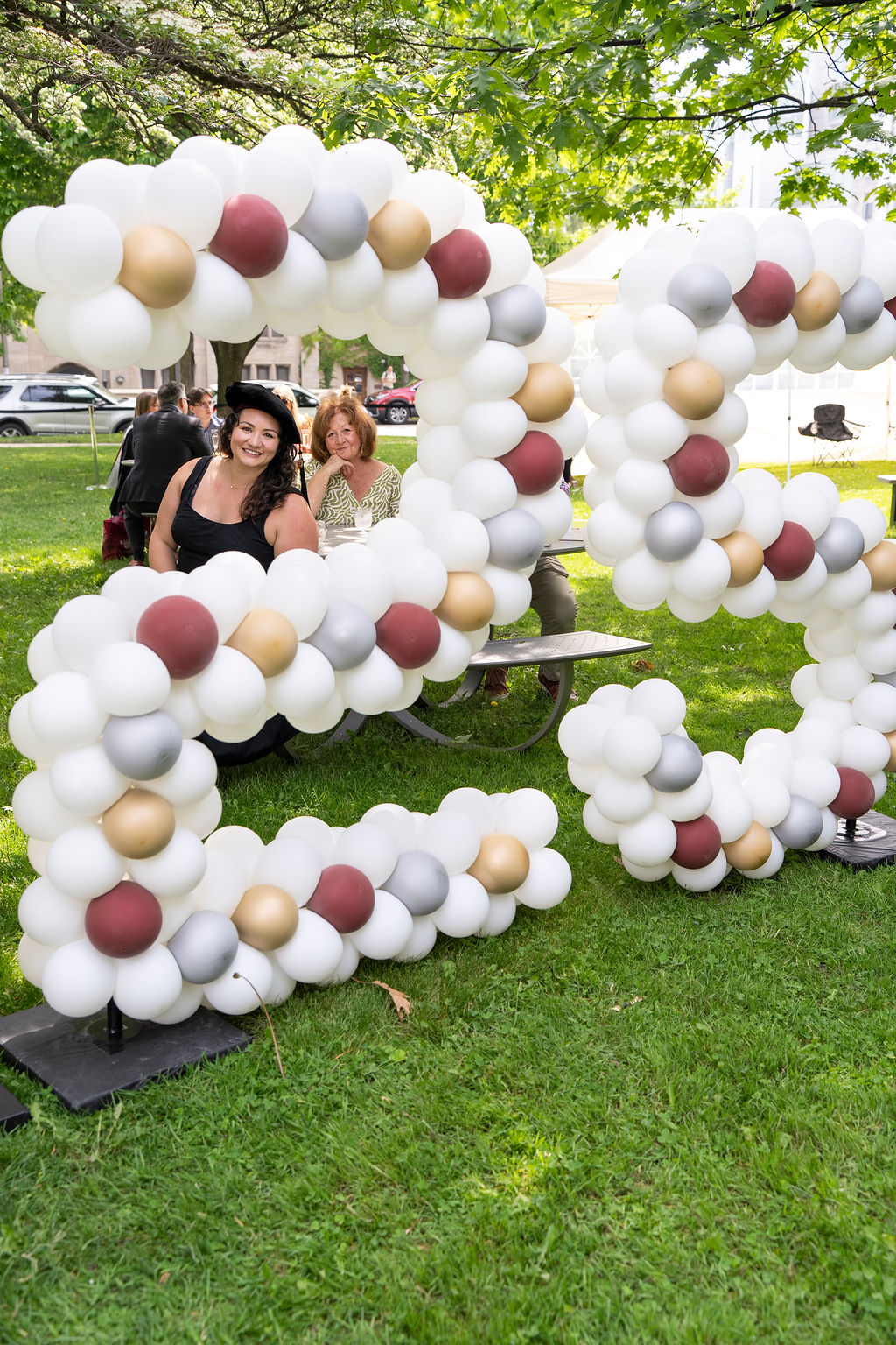 woman in black dress with graduation cap standing behind balloons that is shaped like the number 25