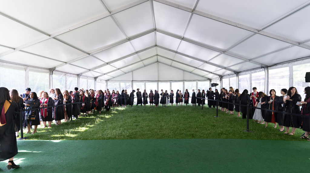 a group of graduates standing in line for processional in grassy area under a tent