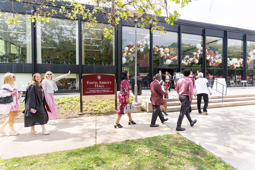 Group of people walking waving and smiling as they enter Edith Abbott Hall where balloons and festivities are behind them