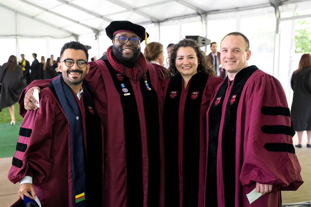 A group of four Doctoral Graduates in maroon regalia smiling 